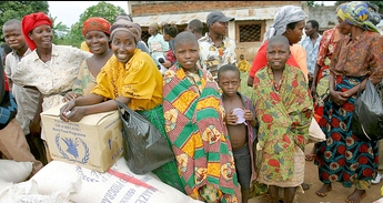 Group of smiling individuals in vibrant traditional African attire, waiting in line to receive aid packages.